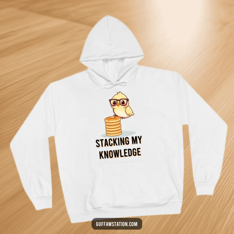A bird wearing glasses precariously balancing a stack of pancakes, printed on a warm and funny hoodie.
